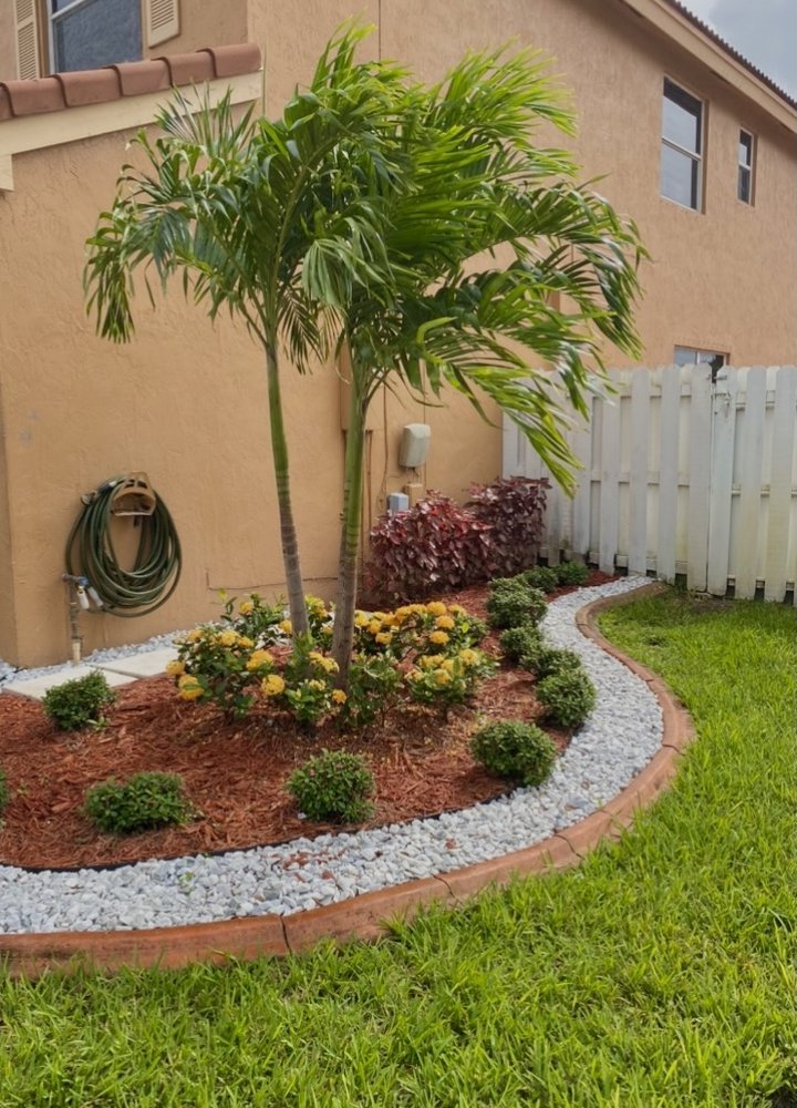 Curved landscape bed with palms, flowers, mulch and decorative stone